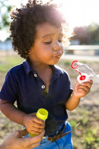 African american baby blowing soap bubbles in the park.